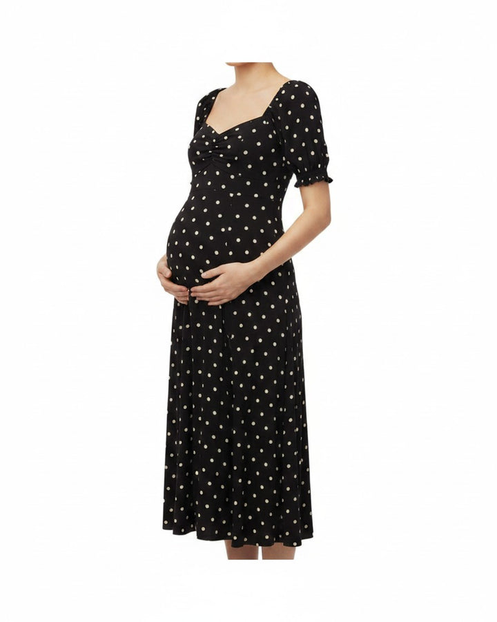 Pregnant woman wearing a Mom & Me Boutique black midi dress with white polka dots, sweetheart neckline, and puff sleeves