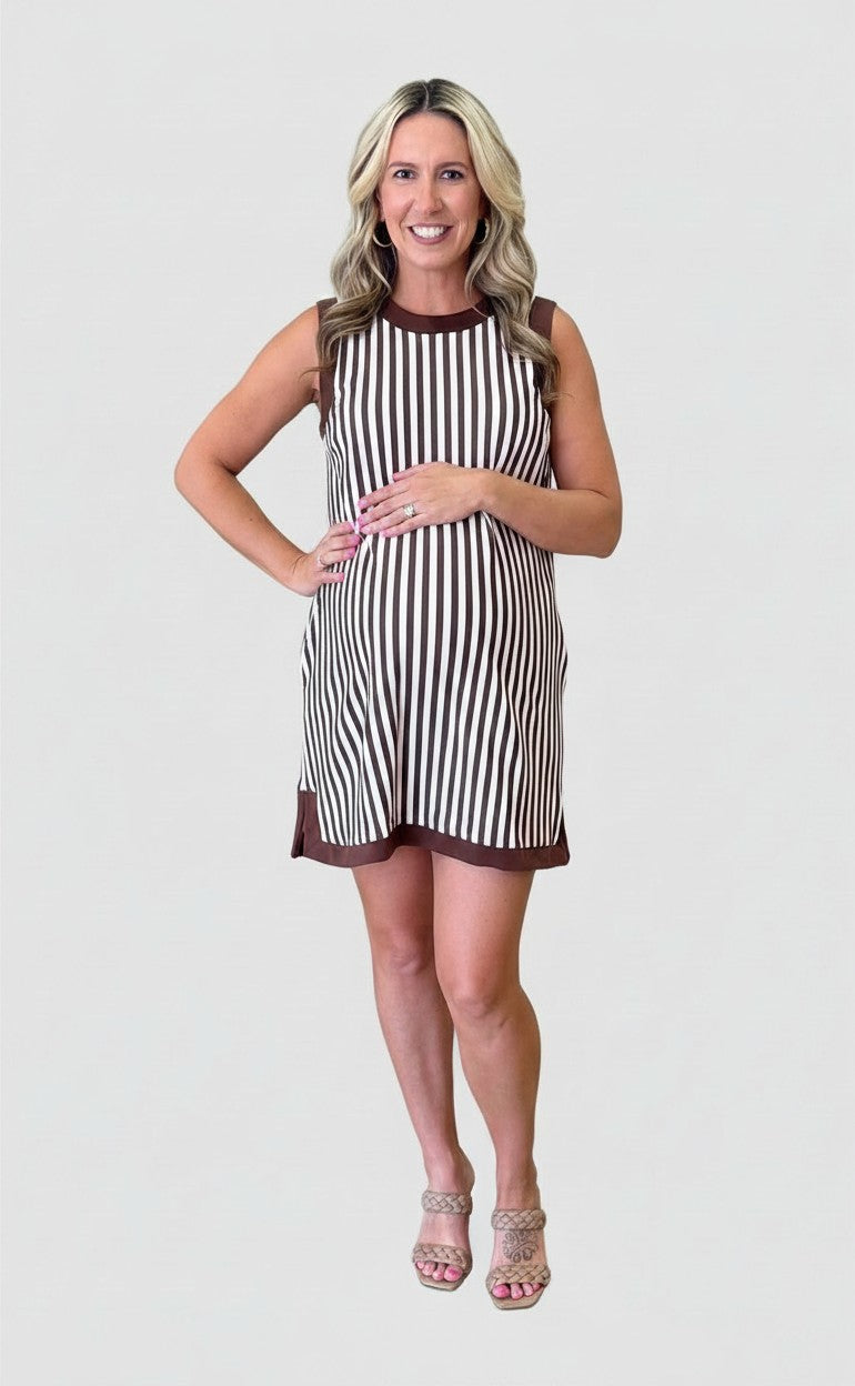 Pregnant woman wearing a Mom & Me Boutique brown and white striped sleeveless Bonnie dress with a solid brown trim.